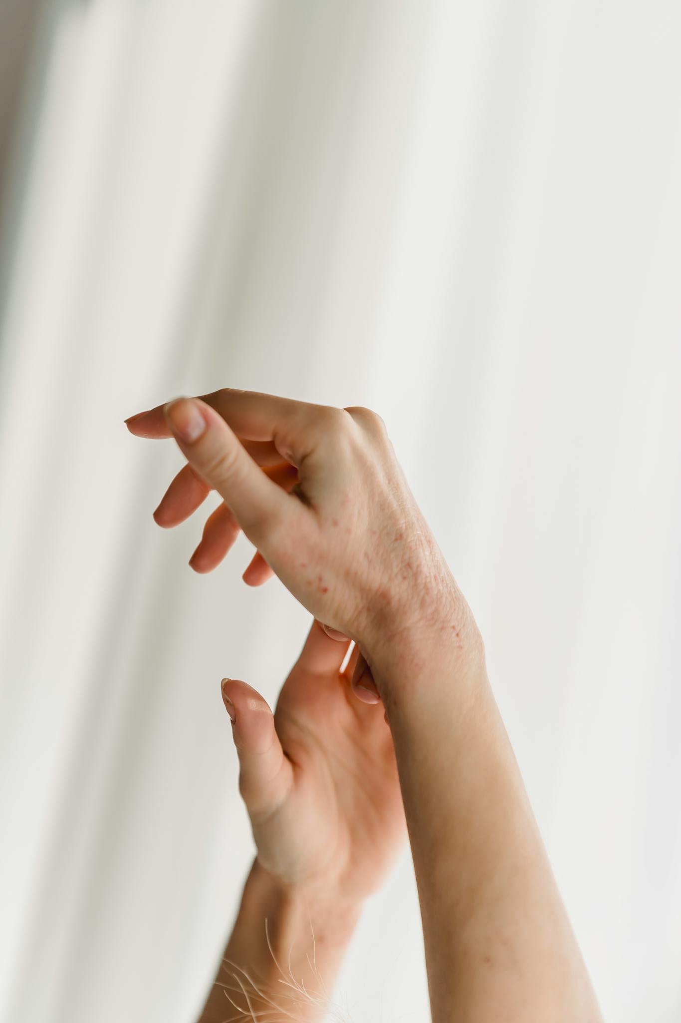A pair of delicate hands gracefully posed against a white curtain backdrop.